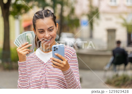 Happy woman counting money dollar cash, use smartphone calculator app in urban city street Happy woman counting money dollar cash, use smartphone calculator app in urban city street 125923428