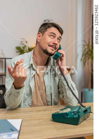 Caucasian man freelancer talking with client on retro old-fashioned wired telephone at table at home 125923462