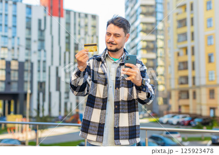 Caucasian man using credit bank plastic card and smartphone shopping online on downtown city street 125923478