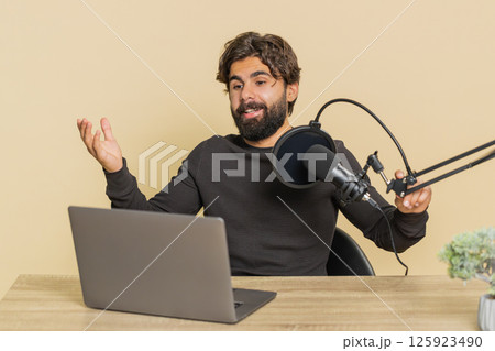 Happy blogger man recording podcast speaking into microphone and laptop webcam on beige background Happy blogger man recording podcast speaking into microphone and laptop webcam on beige background 125923490