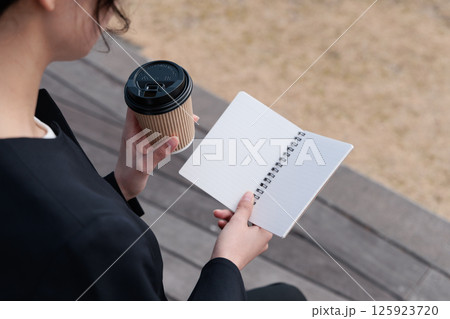 コーヒーを飲みながらメモ帳を眺めるスーツの若い女性 コーヒーを飲みながらメモ帳を眺めるスーツの若い女性 125923720