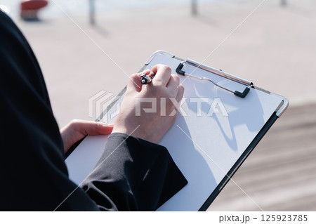 屋外でクリップボードに書き込むスーツ姿の女性 125923785