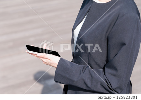 屋外でスマートフォンを操作するスーツの若い女性 屋外でスマートフォンを操作するスーツの若い女性 125923801