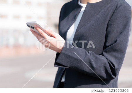 屋外でスマートフォンを操作するスーツの若い女性 125923802