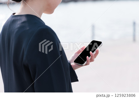 屋外でスマートフォンを操作するスーツの若い女性 125923806