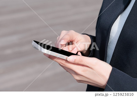 屋外でスマートフォンを操作するスーツの若い女性 125923810