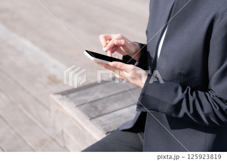屋外でスマートフォンを操作するスーツの若い女性 125923819