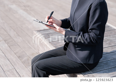 屋外でクリップボードを持つスーツ姿の女性 125923823