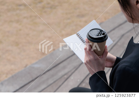 コーヒーを飲みながらメモ帳を眺めるスーツの若い女性 コーヒーを飲みながらメモ帳を眺めるスーツの若い女性 125923877