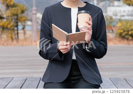 コーヒーを飲みながらメモ帳を眺めるスーツの若い女性 コーヒーを飲みながらメモ帳を眺めるスーツの若い女性 125923878