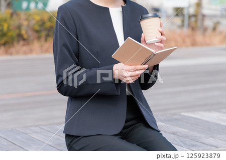 コーヒーを飲みながらメモ帳を眺めるスーツの若い女性 コーヒーを飲みながらメモ帳を眺めるスーツの若い女性 125923879