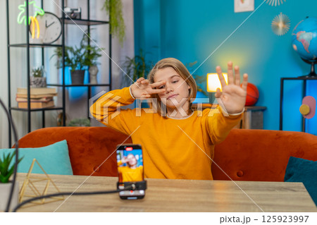 Teenager boy creating trendy selfie videos on smartphone, performing dance moves on couch at home 125923997