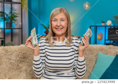 Mature woman joyfully counting dollar money on sofa after lottery win, happy with bonus gift at home Mature woman joyfully counting dollar money on sofa after lottery win, happy with bonus gift at home 125923999