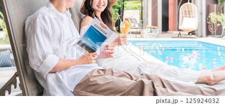 旅行でリゾートホテルのプールサイドのチェアに座るカップル・夫婦 125924032