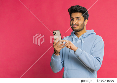 Happy Indian young man browsing social media smiling typing message on smartphone engaging working 125924059