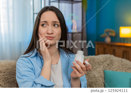 Young woman suffering toothache holding cheek in pain tiredly searching and taking painkiller pills 125924111
