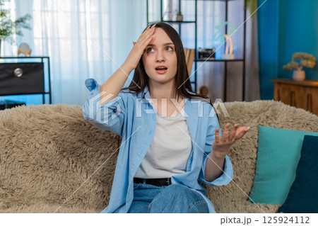 Young woman on sofa upset disappointed doing facepalm gesture frustrated unhappy with mistake 125924112