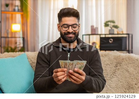 Indian man happily counting cash money on sofa at home, celebrating income or lottery jackpot Indian man happily counting cash money on sofa at home, celebrating income or lottery jackpot 125924129