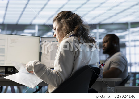 Woman overseeing server room, reading documentation paperwork, troubleshooting hardware. Supervisor doing inspection in server hub, reading technical files at computer desk 125924146
