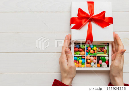 Female hands with delicious candies in box on color background Female hands with delicious candies in box on color background 125924326