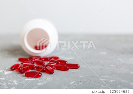 Red pills spilled around a pill bottle. Medicines and prescription pills flat lay background. Red medical capsules 125924625