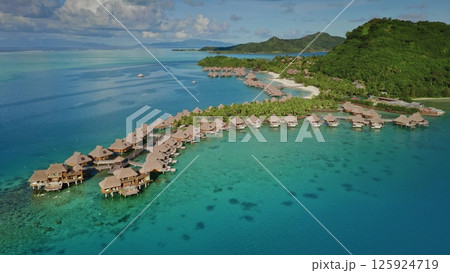 Aerial view zoom out panorama of luxurious overwater bungalows lining the tropical island shore, nestled in vibrant turquoise lagoon in Bora Bora. Popular tourist destination, exotic summer travel 125924719