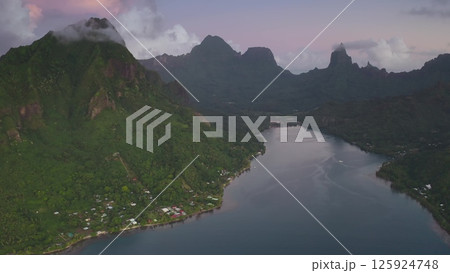 Stunning aerial view lush tropical island with dramatic volcanic peaks, tranquil turquoise water and small coastal village bathed in the warm glow of sunset light. Remote wild nature paradise travel 125924748