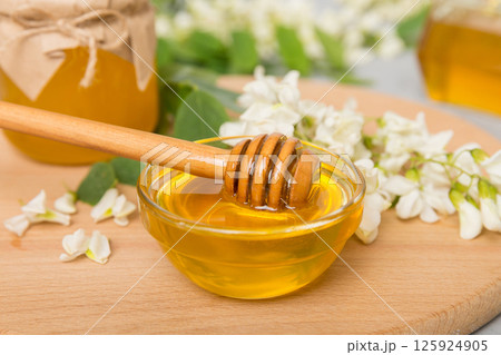 Sweet honey jar surrounded spring acacia blossoms. Honey flows from a spoon in a jar. jars of clear fresh acacia honey on wooden background Sweet honey jar surrounded spring acacia blossoms. Honey flows from a spoon in a jar. jars of clear fresh acacia honey on wooden background 125924905