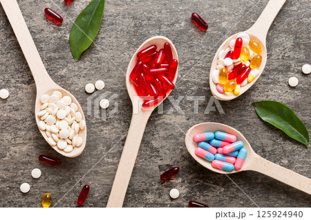 Vitamin capsules in a spoon on a colored background. Pills served as a healthy meal. Red soft gel vitamin supplement capsules on spoon 125924940