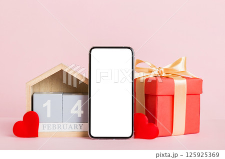 mobile phone with blank screen on colored background with hearts, calendar and gift box, valentine day 14 february concept perspertive view flat lay mobile phone with blank screen on colored background with hearts, calendar and gift box, valentine day 14 february concept perspertive view flat lay 125925369