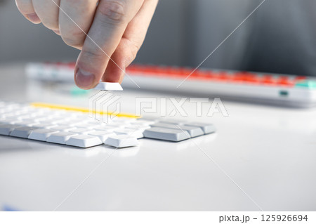 Person removing white keycap from minimalist keyboard during switch maintenance or upgrade 125926694