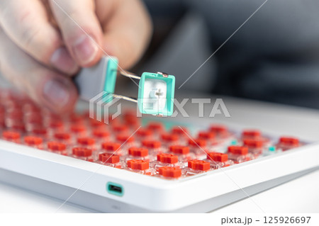Close-up of keycap puller tool removing teal key from red switch mechanical keyboard for modding Close-up of keycap puller tool removing teal key from red switch mechanical keyboard for modding 125926697