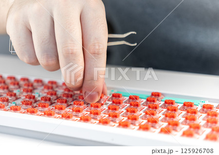 Hand pressing red mechanical switch into keyboard plate with tweezers during custom build Hand pressing red mechanical switch into keyboard plate with tweezers during custom build 125926708