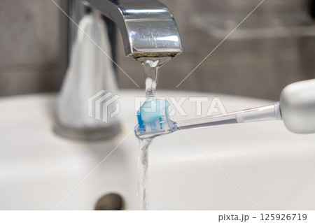 Rinsing electric toothbrush with paste under water for crucial oral hygiene preparation 125926719