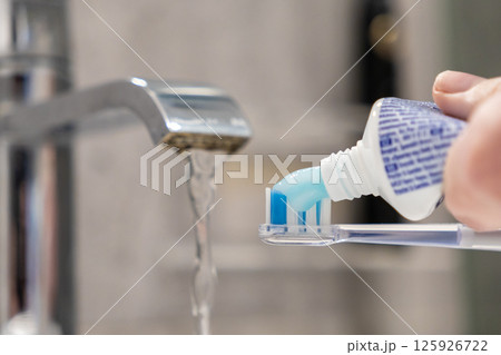 Hand applies toothpaste to electric brush preparing for essential daily oral care 125926722