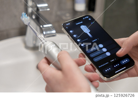 Person controlling smart electric toothbrush via smartphone app for personalized oral health care management 125926726