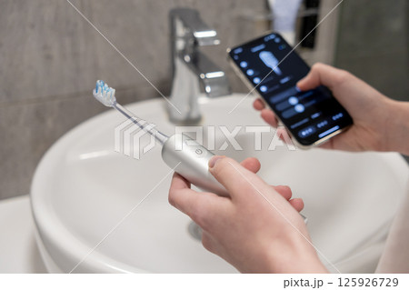 Person controlling smart electric toothbrush via smartphone app for personalized oral health care management 125926729