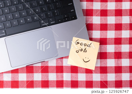 Good job sticky note on a laptop with a checkered tablecloth for work achievement concept 125926747