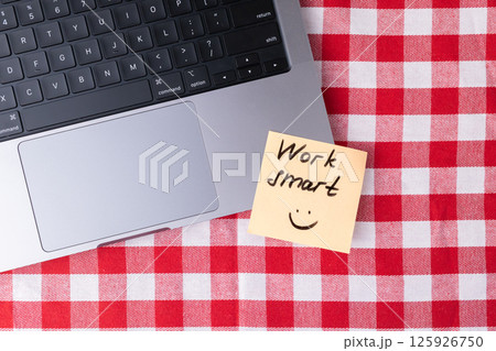 Sticky note with "Work smart" text placed next to laptop on checkered table as a simple productivity reminder 125926750