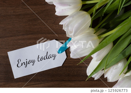 Tag with Enjoy today text attached to white tulips on wooden background perfect for daily motivation inspiration and positive well-being message or spring greetings Tag with Enjoy today text attached to white tulips on wooden background perfect for daily motivation inspiration and positive well-being message or spring greetings 125926773