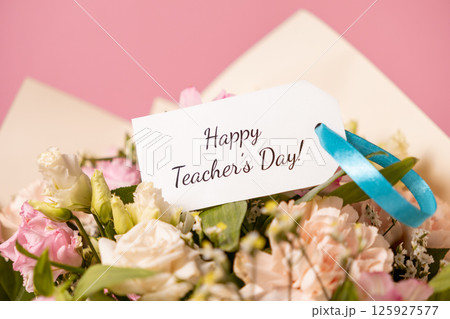 beautiful teachers day bouquet with a handwritten "happy teachers day" message card tied with a blue ribbon, expressing gratitude and appreciation on a soft pink background 125927577