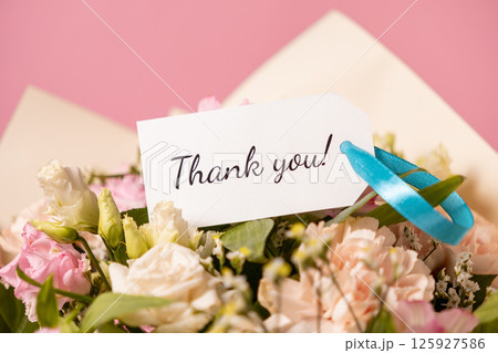 elegant bouquet of pastel flowers with a handwritten thank you message card tied with a blue ribbon, expressing gratitude and appreciation on a soft pink background 125927586