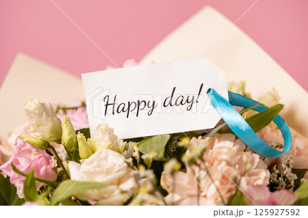 floral bouquet with a cheerful message card tied with a blue ribbon, featuring pastel roses and lisianthus against a soft pink background 125927592