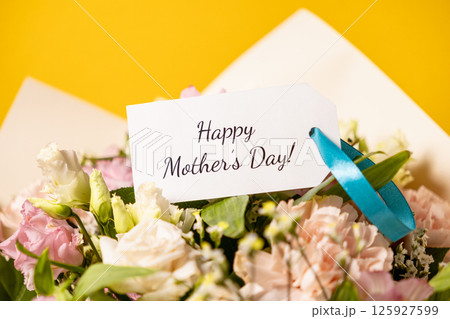 beautiful floral bouquet with happy mother's day message on elegant gift tag, adorned with a soft blue ribbon, set against a warm yellow background for a heartfelt and loving celebration beautiful floral bouquet with happy mother's day message on elegant gift tag, adorned with a soft blue ribbon, set against a warm yellow background for a heartfelt and loving celebration 125927599