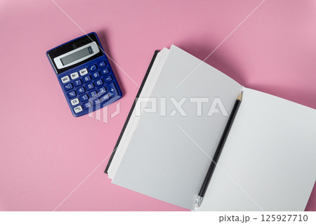 Blue calculator, blank notebook, pencil represent finance, education, strategy on pink background Blue calculator, blank notebook, pencil represent finance, education, strategy on pink background 125927710