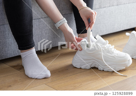 Person's hands inserting white shoe shaper into athletic training sneaker indoors, maintaining shape and freshness for next use 125928899