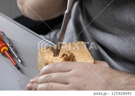 man using a chisel to carve wood during a diy woodworking project, close-up on hands and tools 125928945