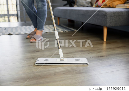 Woman mopping, wiping sleek hardwood floor in modern home setting. Housewife use cleaning mop in cozy living house room. Housekeeping, housework. Sanitation, cleanliness, hygiene, cleanup, maintenance 125929011