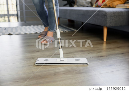 Woman mopping, wiping sleek hardwood floor in modern home setting. Housewife use cleaning mop in cozy living house room. Housekeeping, housework. Sanitation, cleanliness, hygiene, cleanup, maintenance Woman mopping, wiping sleek hardwood floor in modern home setting. Housewife use cleaning mop in cozy living house room. Housekeeping, housework. Sanitation, cleanliness, hygiene, cleanup, maintenance 125929012