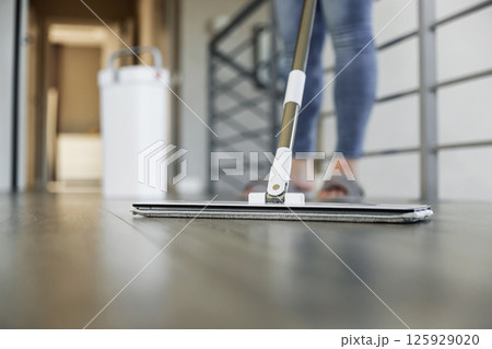 Woman mopping, wiping sleek hardwood floor in modern home setting. Housewife use cleaning mop in cozy living house room. Housekeeping, housework. Sanitation, cleanliness, hygiene, cleanup, maintenance 125929020